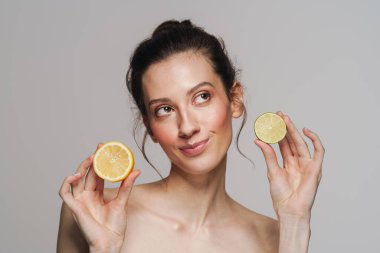 Gülümseyen yarı çıplak kadın gri arka planda limon ve limonla poz veriyor.