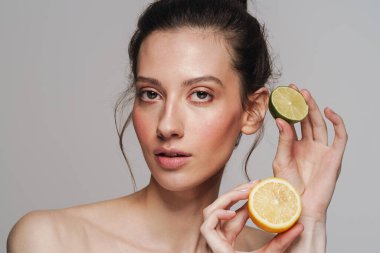 Gri arkaplanda limonla poz veren güzel yarı çıplak kadın.