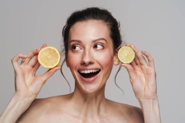 Gri arka planda limon ve limonla poz veren heyecanlı yarı çıplak kadın.