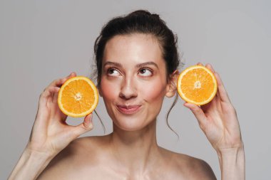 Gülümseyen yarı çıplak kadın gri arka planda izole edilmiş turuncu bir poz veriyor.