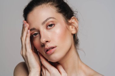 Gri arka planda izole edilmiş güzel yarı çıplak kadın poz veriyor ve kameraya bakıyor.