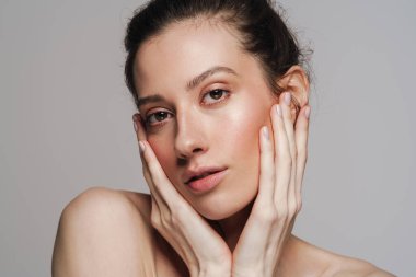 Gri arka planda izole edilmiş güzel yarı çıplak kadın poz veriyor ve kameraya bakıyor.