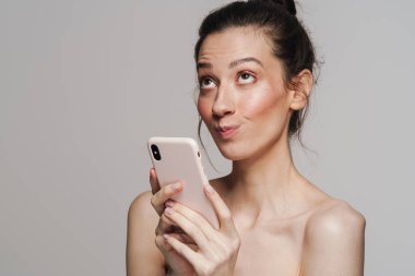 Gri arka planda izole edilmiş cep telefonu kullanan mutlu yarı çıplak kadın.