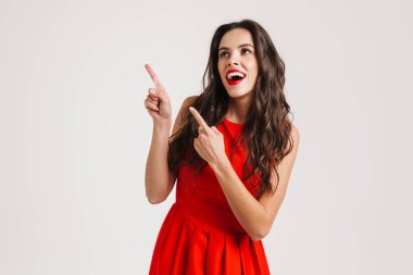 Mutlu, güzel, güzel kız gülümseyen ve parmaklarını yukarıya gösteren pembe arka planda soyutlanmış.