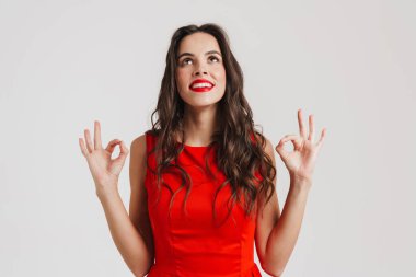 Mutlu güzel güzel kız gülümsüyor ve pembe arka planda iyi bir işaret gösteriyor.