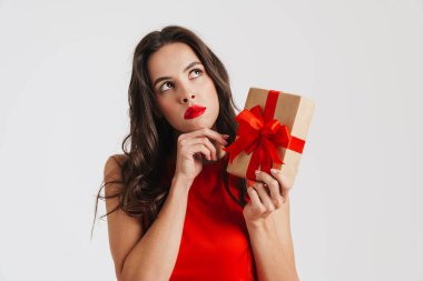 Beyaz arka planda izole edilmiş hediye kutusuyla poz veren kafası karışmış güzel esmer kız.