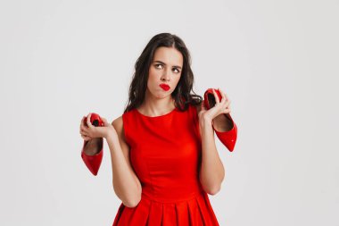 Düşünceli, çekici esmer kız beyaz arka planda izole edilmiş topuklu ayakkabılarla poz veriyor.