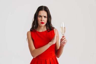Tatminsiz esmer kız beyaz arka planda izole edilmiş şampanyayla poz verirken durduğunu gösteriyor.