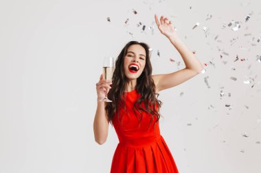 Heyecanlı esmer kız beyaz arka planda izole edilmiş şampanya içerken dans ediyor.