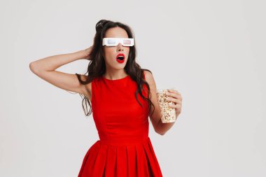 Üç boyutlu gözlüklü güzel bir kız beyaz arka planda izlenmiş bir film izlerken patlamış mısır yiyor.