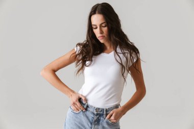 Güzel esmer kız, elleri ceplerinde poz veriyor, beyaz arka planda soyutlanmış.