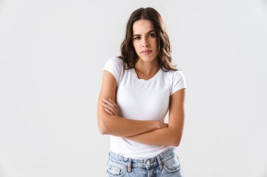 Güzel esmer güzel kız kollarını kavuşturmuş beyaz arka planda yalnız poz veriyor.