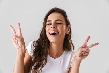 Neşeli güzel kız gülümsüyor ve beyaz arka planda izole edilmiş barış işareti gösteriyor.