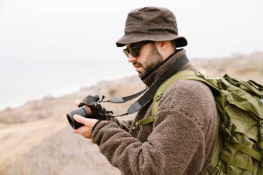 Güneş gözlüklü yakışıklı fotoğrafçı dışarıda dijital kamerayla yürüyor.