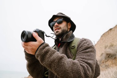 Güneş gözlüklü fotoğrafçı dışarıda dijital kamerada fotoğraf çekiyor.