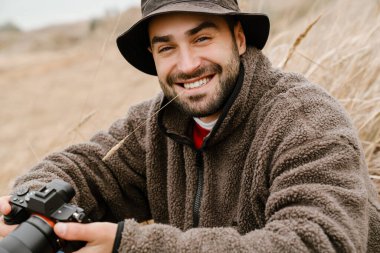 Dışarıda otururken kamerayla gülümseyen mutlu yakışıklı fotoğrafçı.