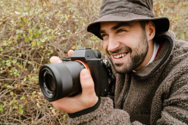 Dışarıdaki dijital kamerada fotoğraf çekerken gülümseyen yakışıklı fotoğrafçı.