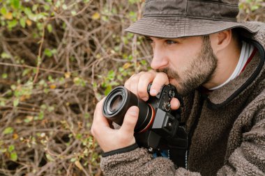Odaklanmış yakışıklı fotoğrafçı düşünür ve dijital kamerayı açık havada tutar.