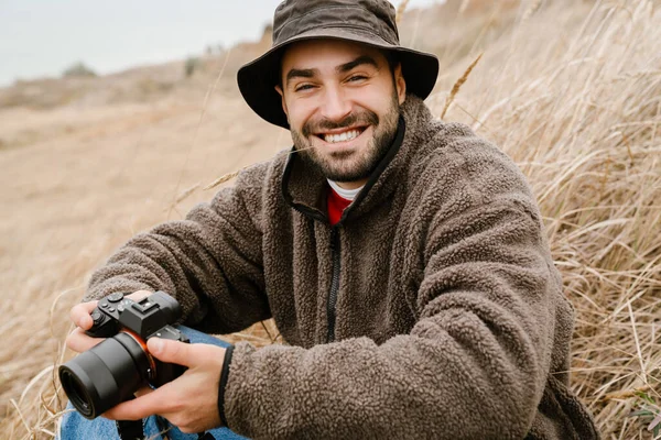 Happy handsome photographer with camera smiling while sitting outdoors