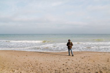 Güneş gözlüklü mutlu fotoğrafçı sahilde dijital kamerayla yürüyor.