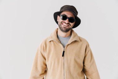 Güneş gözlüklü neşeli yakışıklı adam gülümsüyor ve beyaz arka planda izole edilmiş kameraya bakıyor.