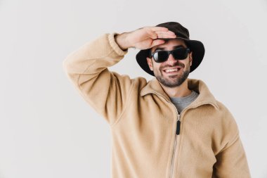 Güneş gözlüklü neşeli yakışıklı adam gülümsüyor ve beyaz arka planda izole edilmiş kameraya bakıyor.