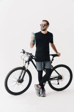 Mutlu sürücü, beyaz arka planda izole edilmiş bisikletiyle poz verirken su içer.