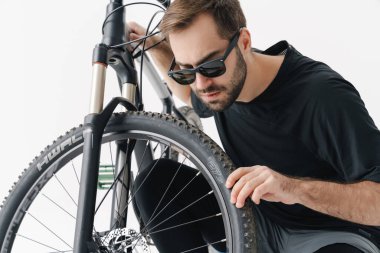 Bisikletini tamir eden yakışıklı bir adam beyaz arka planda izole edilmiş.