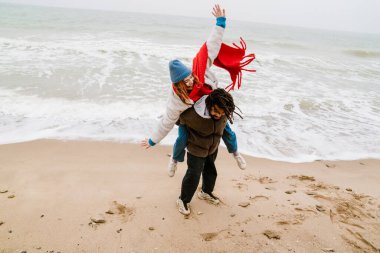 Kumsaldaki mutlu, etnik çeşitliliğe sahip genç çift sıkı bir şekilde sırtlarını sıvazlıyor.