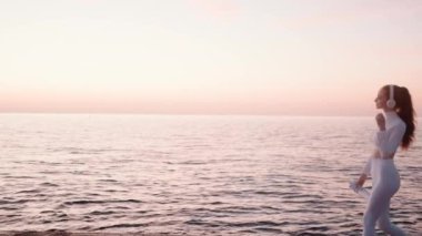 Kulaklık takan çekici kızıl saçlı genç bir kadının yan görüntüsü sabah deniz kenarında yürüyor.