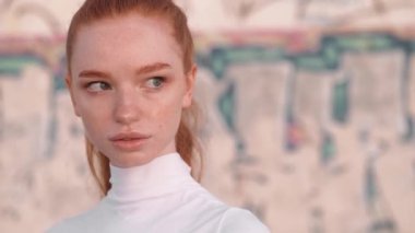 Çekici, genç, kızıl saçlı bir kadının yakın çekim görüntüsü sabah dışarıda kameraya poz veriyor.