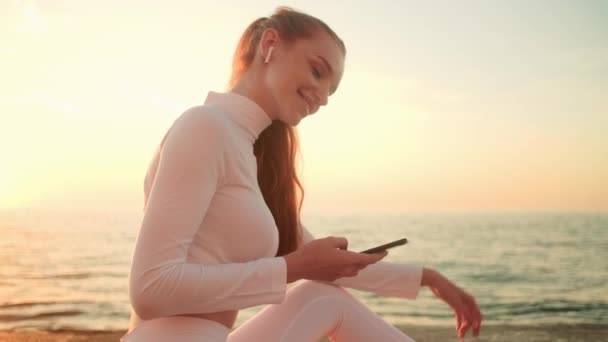 Een Lachende Jonge Vrouw Een Wit Sportpak Gebruikt Haar Mobiele — Stockvideo