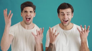 Şok olmuş iki adam kameraya bakıyor. Stüdyonun mavi arka planında izole bir şekilde duruyorlar.