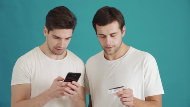 Dwóch Uśmiechniętych Facetów Używa Karty Kredytowej Smartfona Niebieskim Tle Studio — Wideo stockowe
