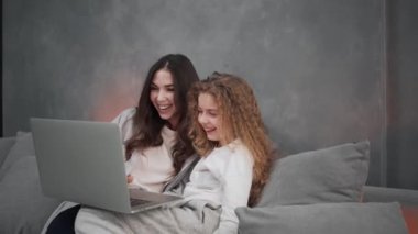 Memnun anne ve kızı evdeki kanepede otururken dizüstü bilgisayar kullanıyorlar.