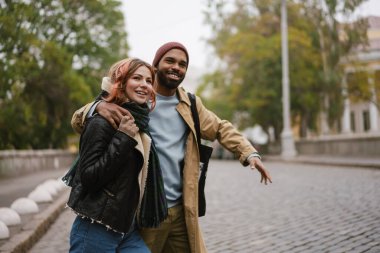 Çok uluslu güzel mutlu çift şehir caddesinde yürürken sarılıp gülüyor.