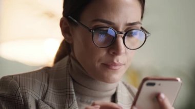 Ofiste otururken gözlüklü bir iş kadınının cep telefonuna yakın çekim görüntüsü