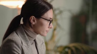 Gözlüklü ciddi bir iş kadını ofiste bilgisayarını kullanıyor.