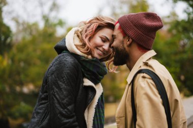 Çok uluslu mutlu çift gülümserken, şehir caddesinde kafa kafaya duruyorlar.
