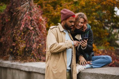 Şehir caddesinde sarılıp cep telefonu kullanan çok uluslu bir çift.