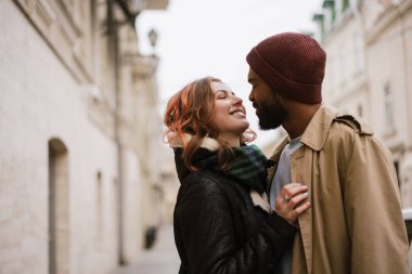 Çok uluslu, güzel, mutlu bir çift şehirde yürürken sarılıyor ve gülümsüyor.