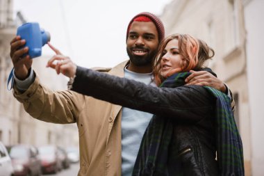 Çok uluslu gülümseyen bir çift şehrin sokaklarında selfie çekiyor ve sarılıyor.