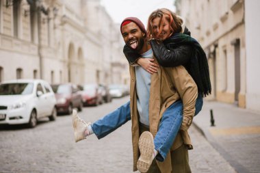 Mutlu Afro-Amerikalı adam, gülen kız arkadaşını sırtında taşıyor.