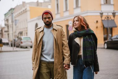 Şehir caddesinde yürürken el ele tutuşan çok uluslu güzel bir çift.