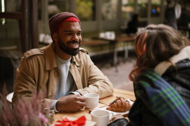 Sokak kafesinde kahve içerken gülümseyen çok uluslu mutlu bir çift.