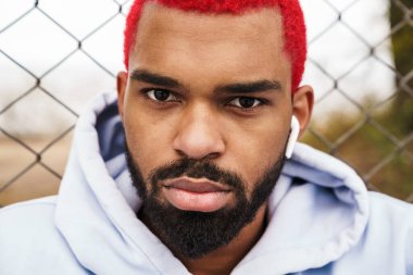 Kablosuz kulaklıklı, dışarıdaki kameraya bakan kendine güvenen Afro-Amerikan adam.