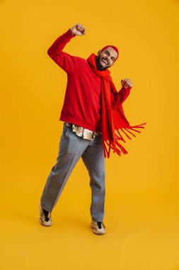 Heyecanlı mutlu Afrikalı adam sarı arka planda izole edilmiş, uzun boylu bir eşarbı kutluyor.