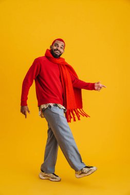 Heyecanlı mutlu Afrikalı adam sarı arka planda soyutlanmış, uzun boylu atkı takıyor.