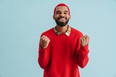 Heyecanlı Afrikalı Amerikalı adam bağırıyor ve sarı arka planda izole edilmiş kazanan hareketi gösteriyor.