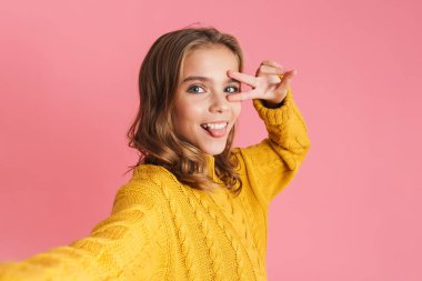 Heyecanlı güzel kız pembe arka planda izole edilmiş selfie çekerken barış işareti yapıyor.